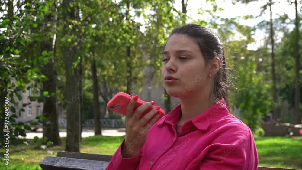 beautiful girl records voice messages on a pink smartphone in a city park in summer. beautiful girl records voice messages on a pink smartphone in a city park in summer.