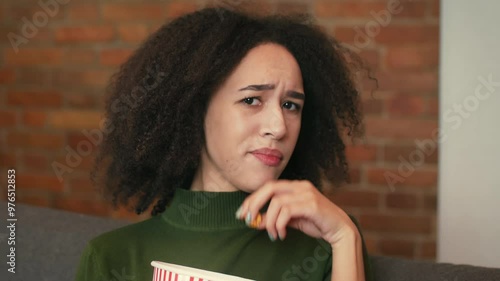 Disgusting tv program. Close up portrait of displease black woman watching show at home and eating popcorn, expressing negativity, slow motion