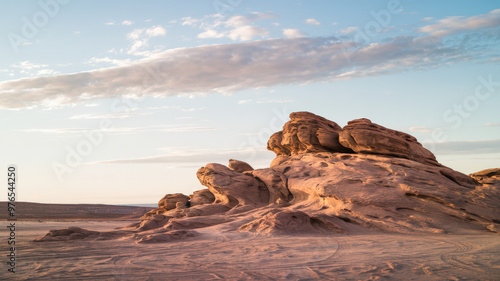 A photo of a vast desert landscape with a lot of negative space. In the foreground, there is a large rock formation with unique shapes. The sky is clear with a few clouds. The horizon line is visible,