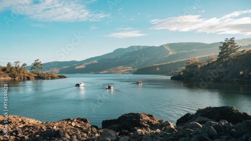 A cinematic shot of a serene landscape with a vast body of water and a few small boats on the water. There are mountains in the background with a few trees. The sky is clear with a few clouds.