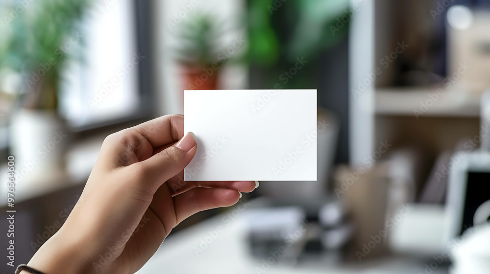 A hand holds a blank white business card in a modern office setting. A hand holds a blank white business card in a modern office setting.