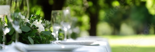 The image shows an elegantly set outdoor dining table with glasses, plates, and floral decorations, likely prepared for a wedding or formal event amidst lush greenery.