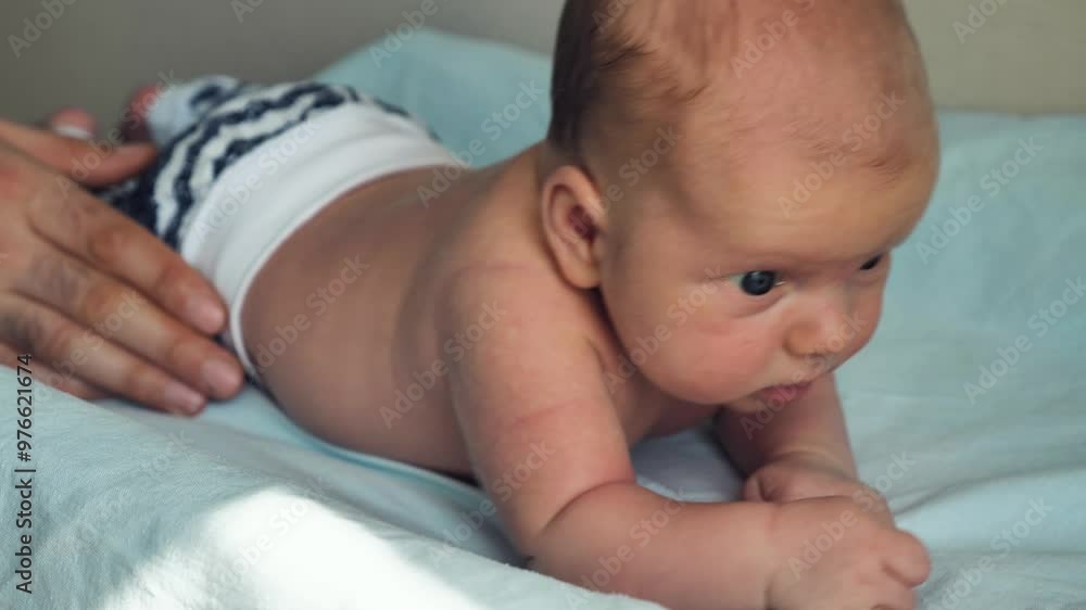 A newborn baby lying on its stomach and trying to hold its head. Close-up. A parent's hand is supporting the baby from the side so that he does not turn over A newborn baby lying on its stomach and trying to hold its head. Close-up. A parent's hand is supporting the baby from the side so that he does not turn over