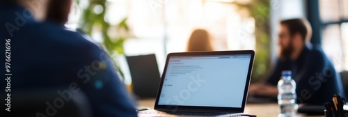 A person working on a laptop in a modern office setup with colleagues in the background, depicting productivity, contemporary work environments, and focus on tasks. photo