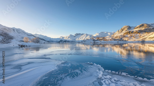 Icy lake surrounded by snow-covered mountains with a clear blue sky at sunrise