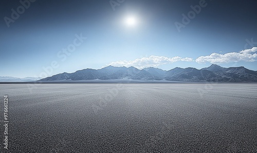 A wide, flat, dry lakebed stretches out towards a range of mountains under a clear blue sky. photo