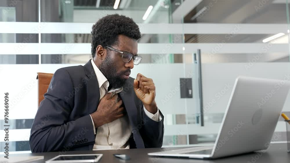 African American businessman coughing while sitting at workplace in business office. Sick with cold or flu employee in a formal suit feels bad, holds his hand to his chest. Black man has a bronchitis African American businessman coughing while sitting at workplace in business office. Sick with cold or flu employee in a formal suit feels bad, holds his hand to his chest. Black man has a bronchitis
