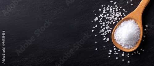 Close-up of coarse salt in a wooden spoon on a dark surface, showcasing the texture and shine of the salt crystals.