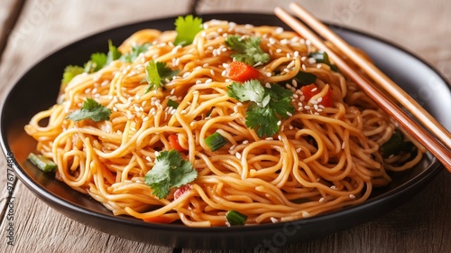 92. High-angle view of a plate of spicy vegetable Hakka noodles, served with wooden chopsticks, garnished with sesame seeds and fresh cilantro