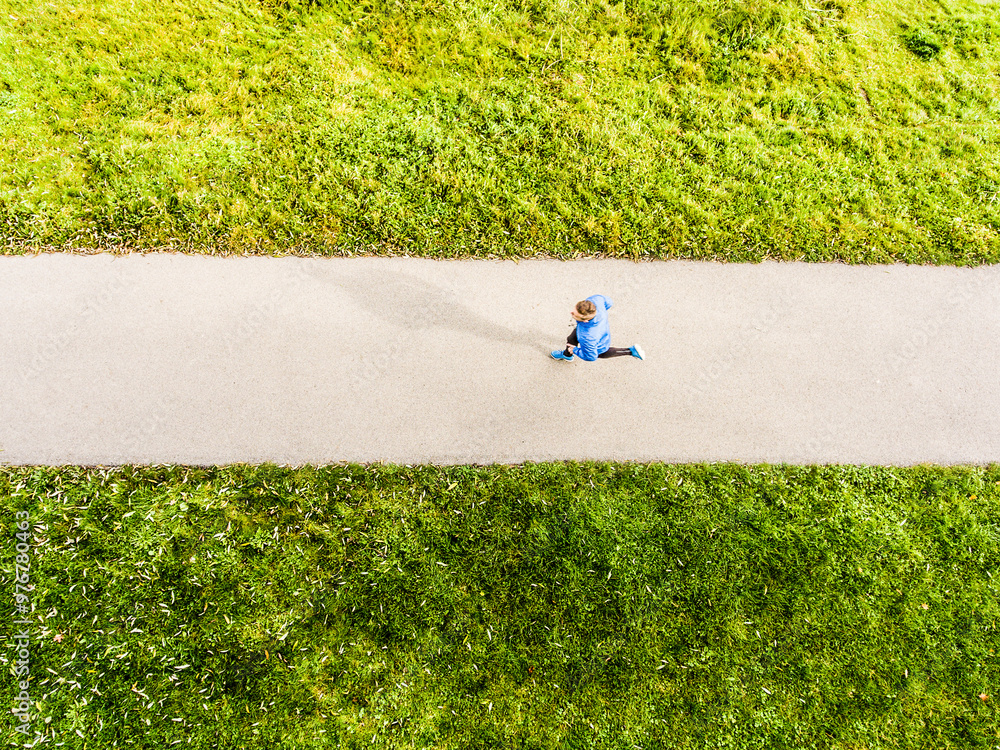 Fototapeta premium Aerial view of a runner running through autumn park on jogging path. Morning running training.
