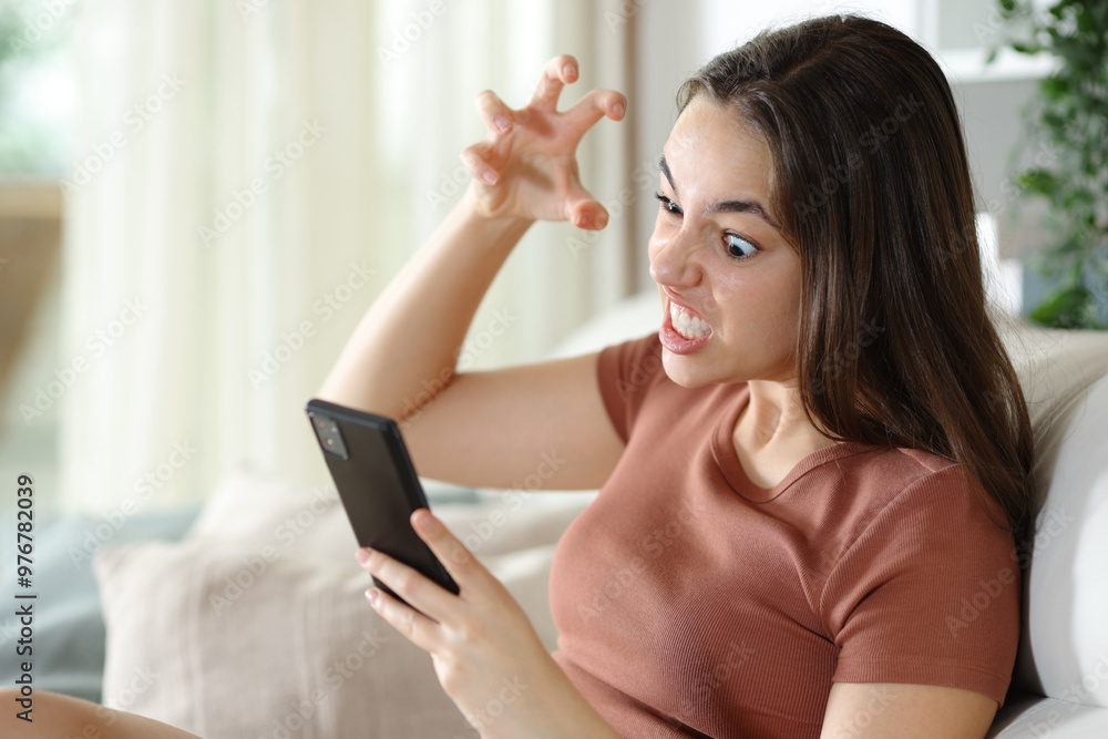 Angry woman checking smart phone sitting at home Angry woman checking smart phone sitting at home