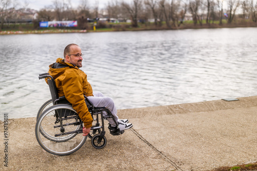 Happy paraplegic handicapped man in wheelchair by the lake. He is rolling on walkway.