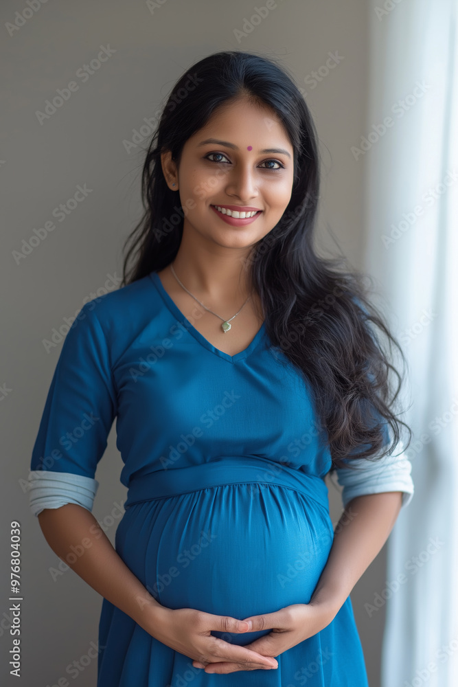 A pregnant woman is smiling and wearing a blue dress. She is holding her stomach and looking at the camera A pregnant woman is smiling and wearing a blue dress. She is holding her stomach and looking at the camera
