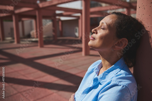 Relaxed woman enjoying sunlight with eyes closed in an urban outdoor setting, embracing tranquility and mindfulness photo