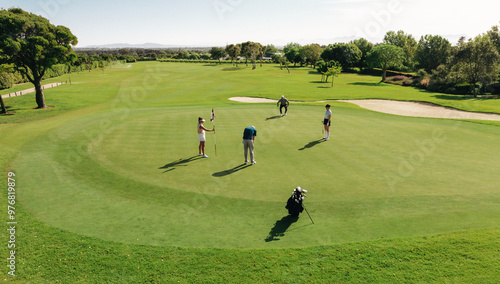 Golf group playing golf from the green at a sunny golf course surrounded by sand bunkers