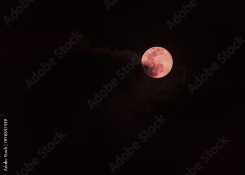 A image of a blood moon rising. The moon, a vibrant crimson hue, is partially obscured by clouds, creating a dramatic and mystical scene. Perfect for projects related to astronomy, or the supernatural