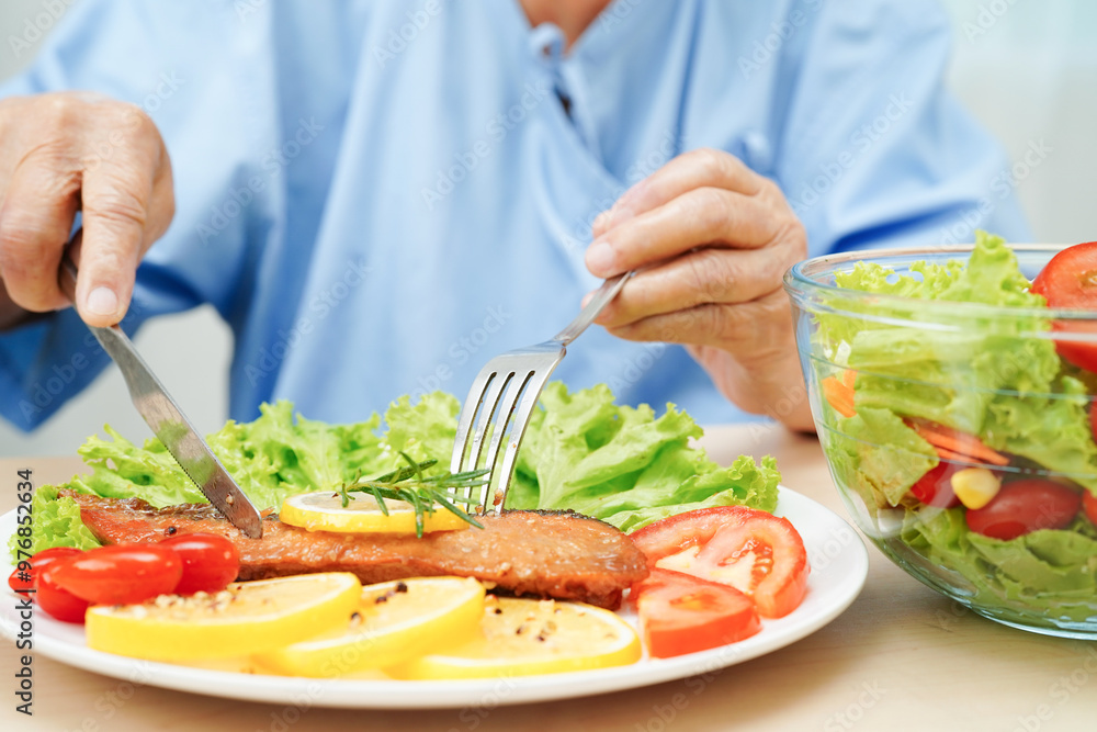 Asian elderly woman patient eating salmon stake and vegetable salad for healthy food in hospital. Asian elderly woman patient eating salmon stake and vegetable salad for healthy food in hospital.