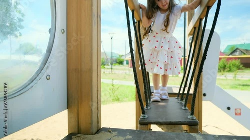 4k footage of funny toddler girl climbing on wooden stapladder on children playground at park photo