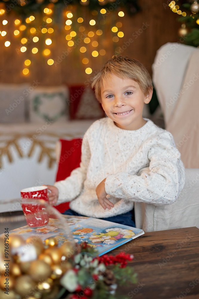 Cute blond child, boy, celebrating Christmas at home, decorated room for the holidays, child reading book and playing Cute blond child, boy, celebrating Christmas at home, decorated room for the holidays, child reading book and playing