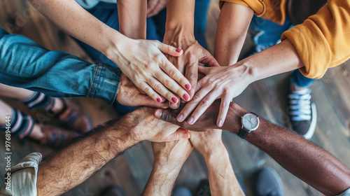 A multinational team of office colleagues fold their arms in the center to show teamwork and support