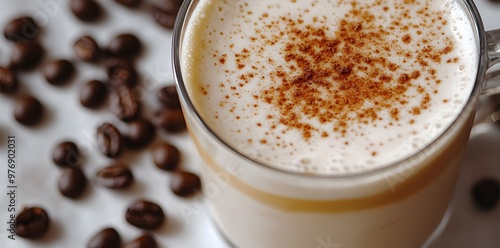 Close-up of a glass of creamy latte with cinnamon sprinkled on top, surrounded by coffee beans