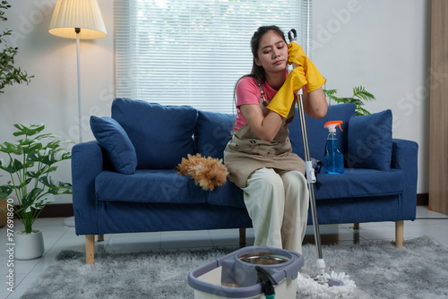 Картината върху платно Tired Asian housewife after doing housework, home office, sitting on the floor in living room near sofa with products, home cleaning supplies, interior design concept, cleaning