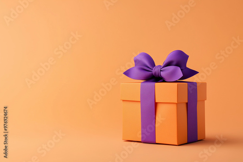 Orange colored gift box with a purple bow on an orange background. Halloween style gift box.  photo