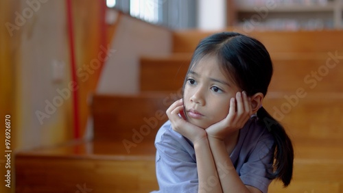 An Asian girl sits on the stairs with a bored expression on her face. Her dim eyes reflect her disinterest in her surroundings.