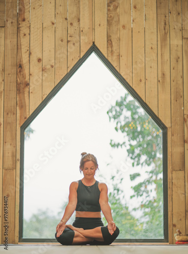 Woman doing Vinyasa yoga pose close to a window with black fitness outfit wooden room natural light photo