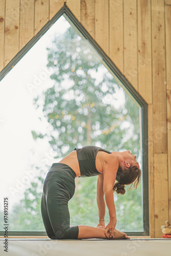 Woman doing vinyasa yoga Camel
Pose beautiful wooden interior photo