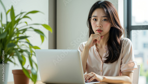 A focused woman working on a laptop in a bright, modern office space with a green plant nearby.