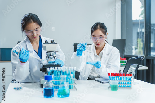 Two Asian women in a lab work on food research, using a microscope, petri dish, and test tubes filled with chemical solutions. They study vegetables, pork, and plants for GMO traits and nutrition.