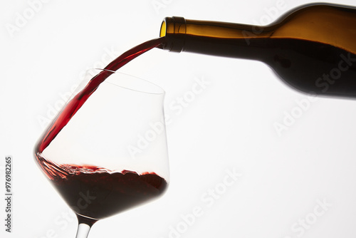 Red wine pouring into tilted wineglass from bottle. photo