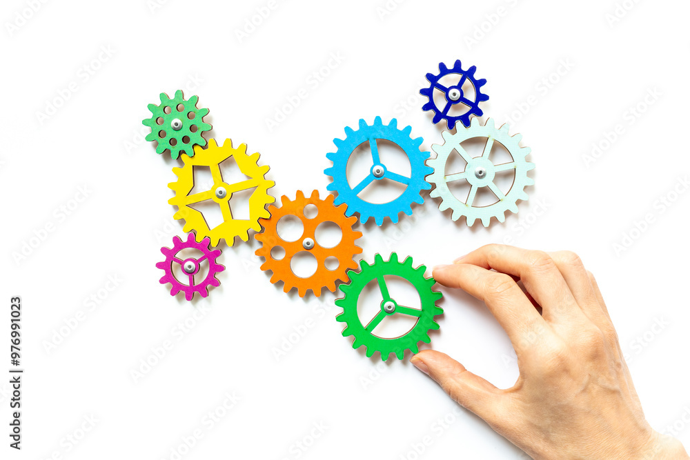 Hand is adding a cog wheel to a chain of gears. Idea or solution concept Hand is adding a cog wheel to a chain of gears. Idea or solution concept