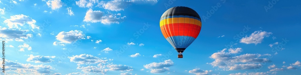 Fototapeta premium Colorful hot air balloon ascends in blue sky with scattered clouds