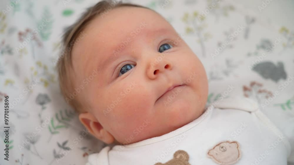 An adorable baby lies on a soft patterned blanket, gazing curiously with bright blue eyes, exploring the world around them An adorable baby lies on a soft patterned blanket, gazing curiously with bright blue eyes, exploring the world around them