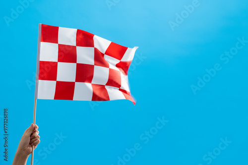 Human hand waving checkered flag on blue background