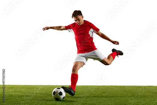 Young athletic man, football player, in red-white uniform, practicing powerful kick on green field against white studio background. Concept of championship, sport events, final game. Ad