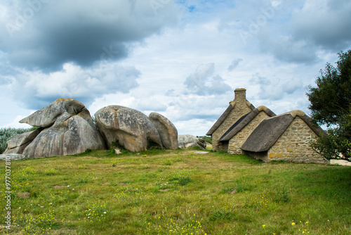 Old stone house with thatched roof and green meadow under cloudy sky in Menehan, Bretagne, France