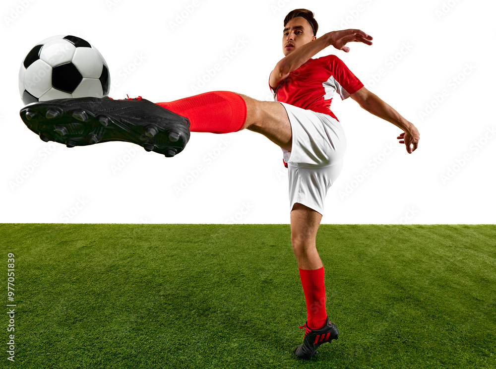 Dynamic shot of football player, dressed in red and white, focuses on powerful kick during training on green field against white background. Game-winning skills. Concept of sport events, final game. Dynamic shot of football player, dressed in red and white, focuses on powerful kick during training on green field against white background. Game-winning skills. Concept of sport events, final game.