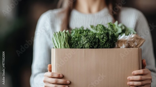 A person holds a box full of fresh vegetables like parsley, string beans, and other greens, alluding to healthy living, organic produce, and sustainable eating habits. photo