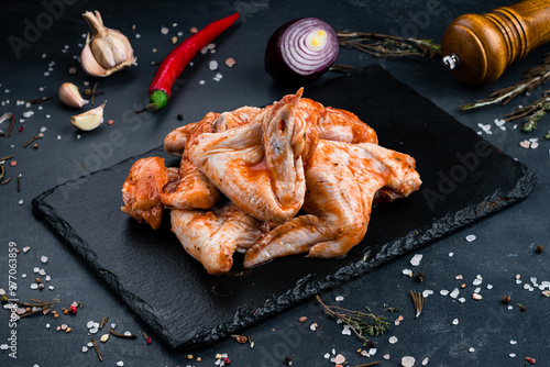 Portion raw marinated barbecue chicken wings in sauce and spices on a dark background.