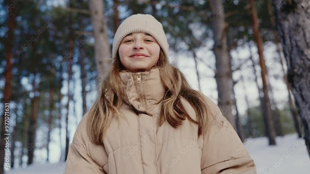 A joyful young girl wearing a beige jacket and white beanie smiles warmly in a snow-covered forest, capturing the essence of winter fun and innocence. A joyful young girl wearing a beige jacket and white beanie smiles warmly in a snow-covered forest, capturing the essence of winter fun and innocence.