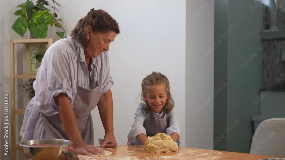 Happy girl kneading pastry dough on table while baking with grandmother at home. Little female child is learning baking from elderly woman, baking concept Happy girl kneading pastry dough on table while baking with grandmother at home. Little female child is learning baking from elderly woman, baking concept