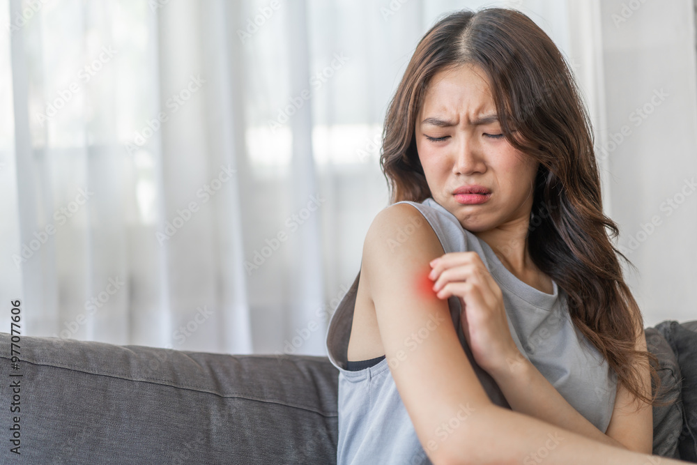 Asian woman with a disgusted expression touching her arm, feeling discomfort or itchiness on a sofa, health and skin irritation issue, unpleasant feeling, young female showing reaction of sensitivity Asian woman with a disgusted expression touching her arm, feeling discomfort or itchiness on a sofa, health and skin irritation issue, unpleasant feeling, young female showing reaction of sensitivity