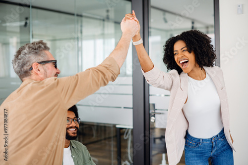 A high-five moment captures the joyful success within a team, as a woman beams with pride and a colleague applauds, showcasing a supportive and uplifting office culture. Value of team achievements