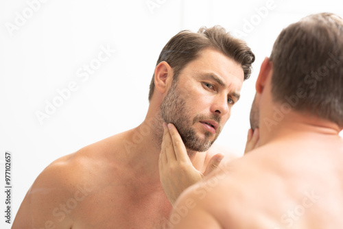 sexy man with stubble looks at the wrinkles on his face. Close up man looking in mirror, sensitive skin, cosmetology treatment. Skin care. joyful, virile, manly, attractive, naked, unshaven, handsome