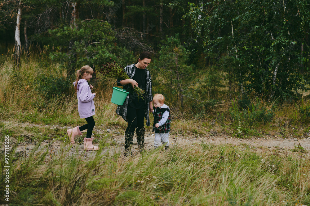 Fototapeta premium Happy family on a walk in the forest picking berries and herbs, traveling along paths and stones mom dad and children