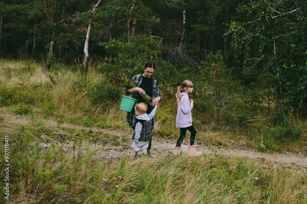 Fototapeta premium Happy family on a walk in the forest picking berries and herbs, traveling along paths and stones mom dad and children