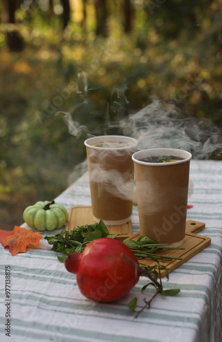 autumn hot healthy drink. autumn picnic in the forest. on the table are two tall paper glasses with tea, next to pomegranates, pumpkins and autumn leaves